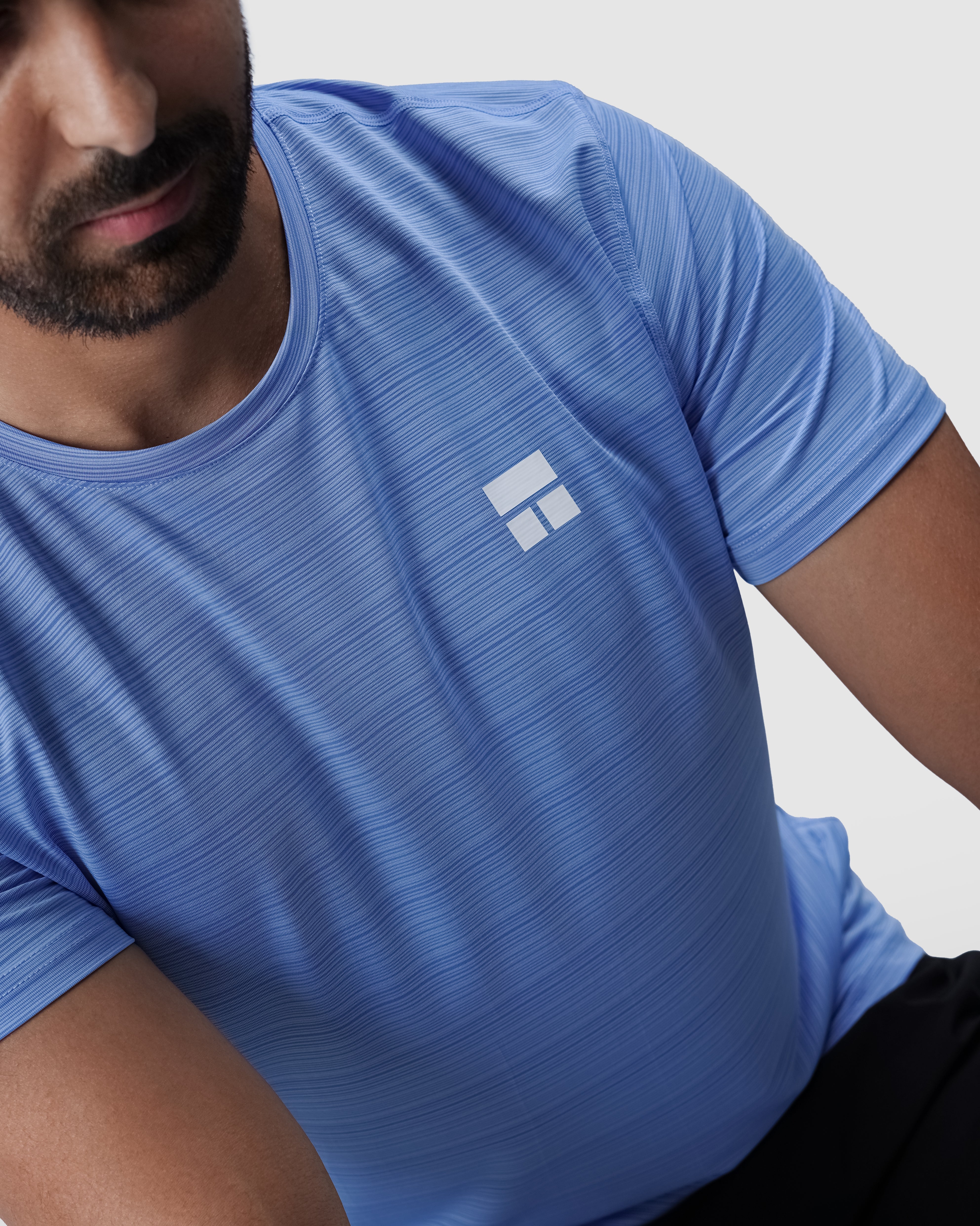 Man wearing a blue athletic shirt with a logo on a light gray background