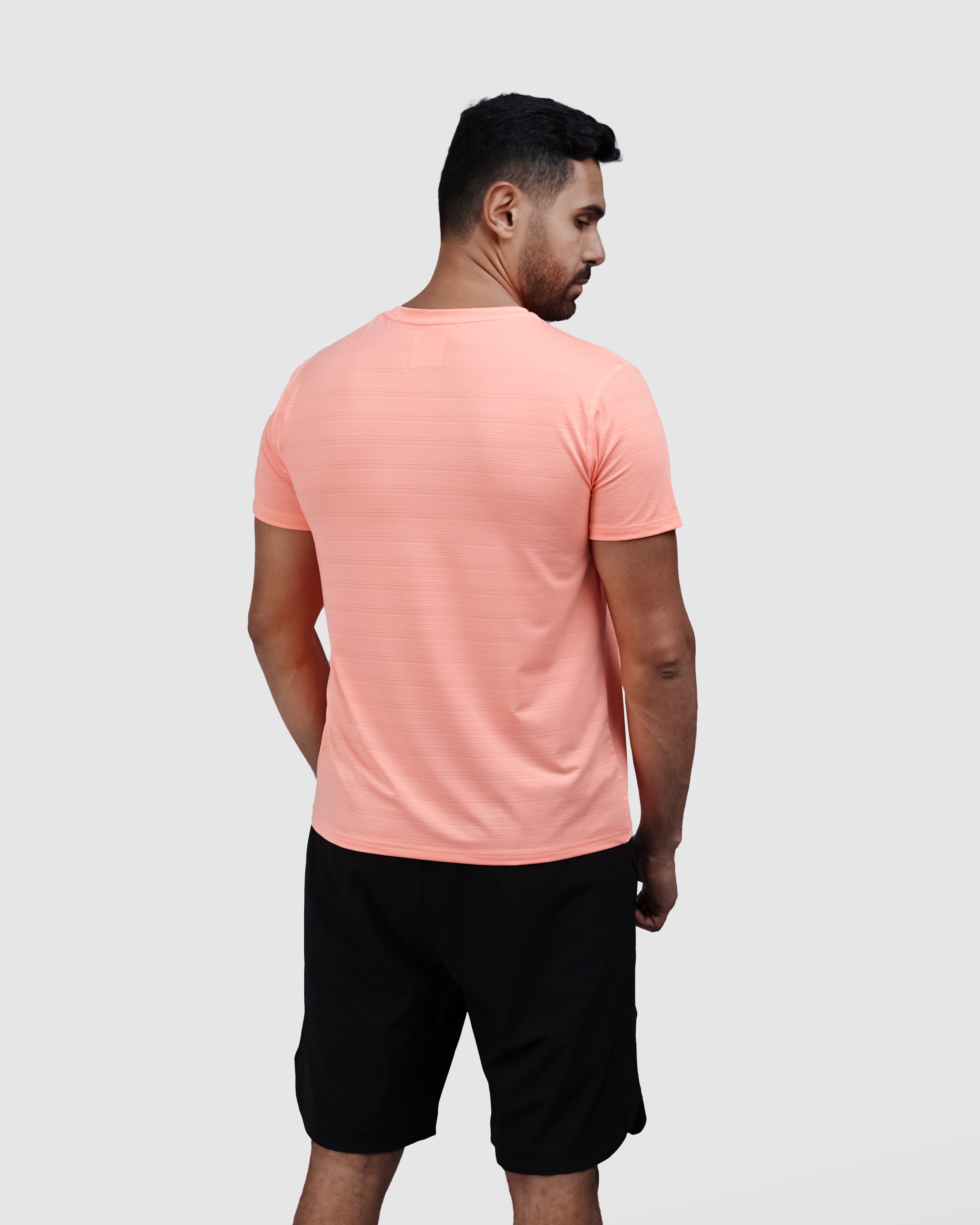 Man wearing a peach t-shirt and black shorts on a white background