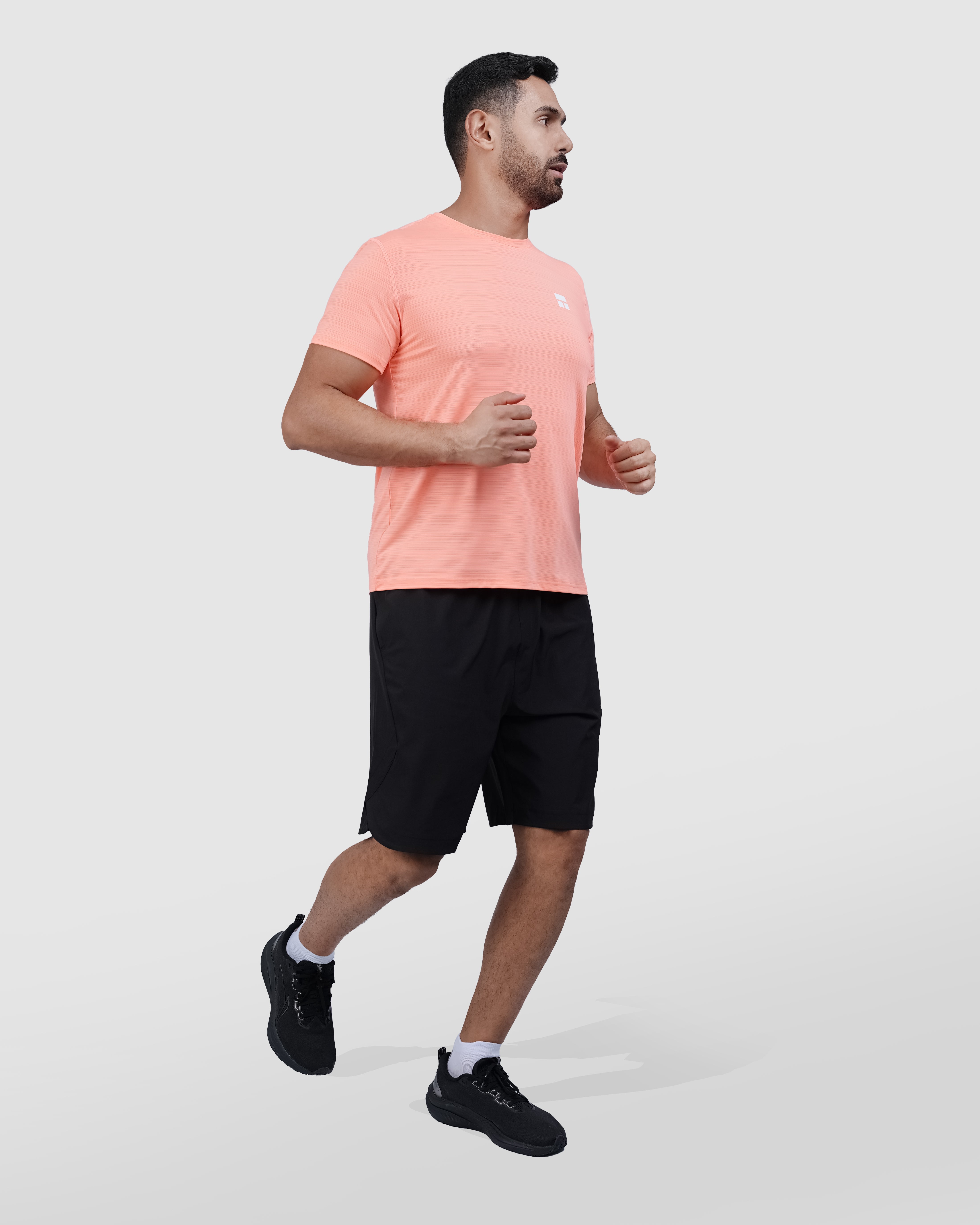 Man wearing a peach t-shirt and black shorts on a white background