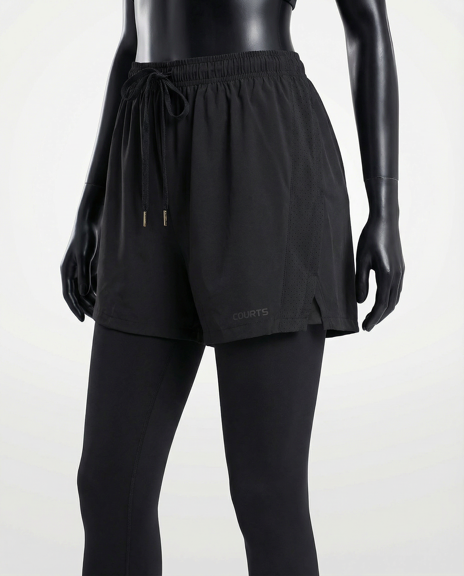 Mannequin wearing black athletic shorts and leggings with white sneakers on a light gray background