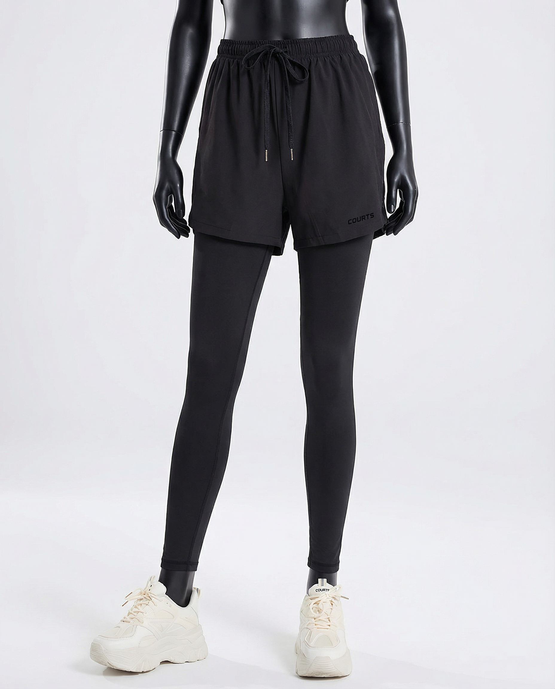 Mannequin wearing black athletic shorts and leggings with white sneakers on a light gray background