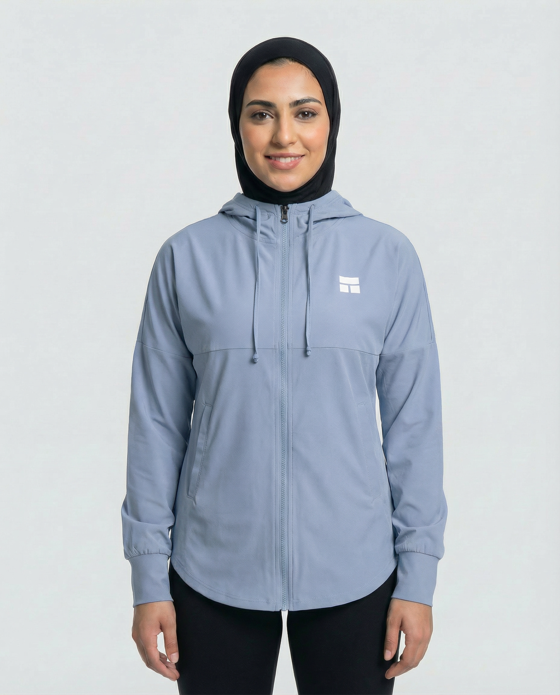 Woman wearing a light blue jacket with a logo on a white background
