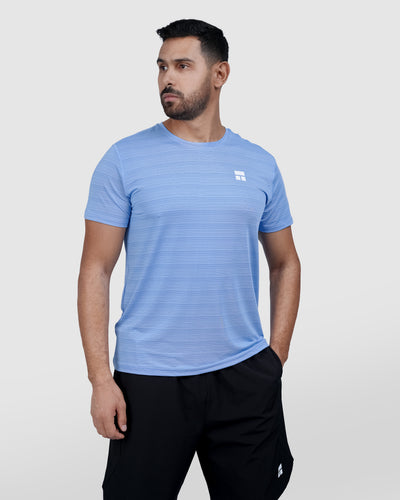 Man wearing a blue athletic shirt with a logo on a light gray background
