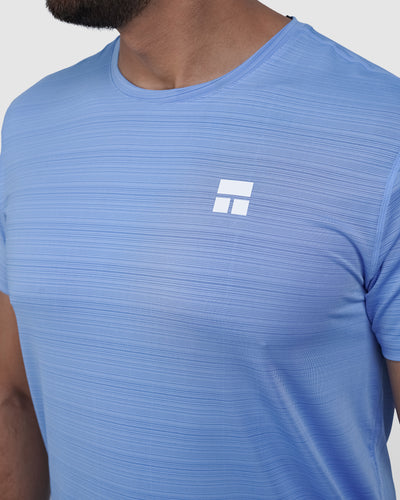 Man wearing a blue athletic shirt with a logo on a light gray background
