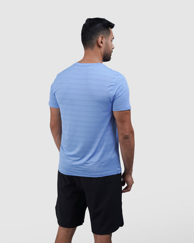 Man wearing a blue athletic shirt with a logo on a light gray background
