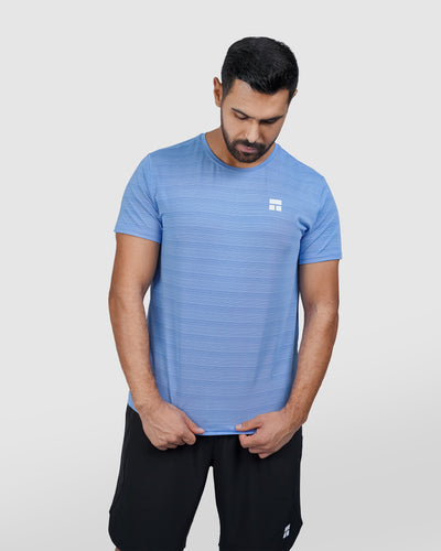 Man wearing a blue athletic shirt with a logo on a light gray background
