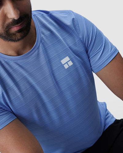 Man wearing a blue athletic shirt with a logo on a light gray background
