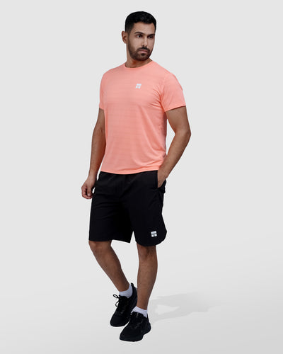 Man wearing a peach t-shirt and black shorts on a white background
