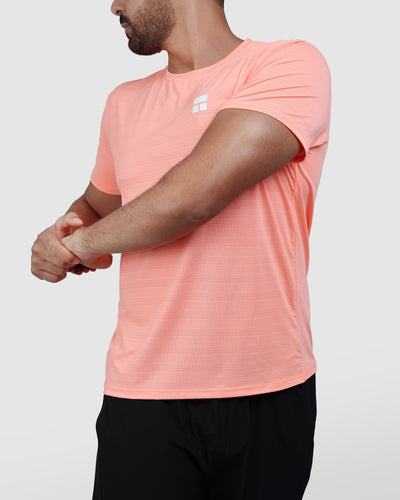 Man wearing a peach t-shirt and black shorts on a white background
