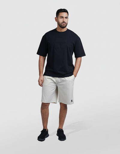 Man wearing a black t-shirt and light gray shorts on a white background

